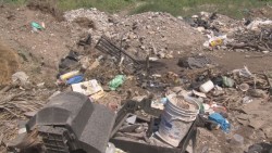 Lote baldío lleno de basura, maleza, inodoro y hasta partes de televisiones