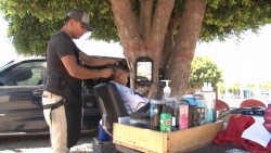Bajo un árbol joven trabaja como barbero para sacar adelante a su familia